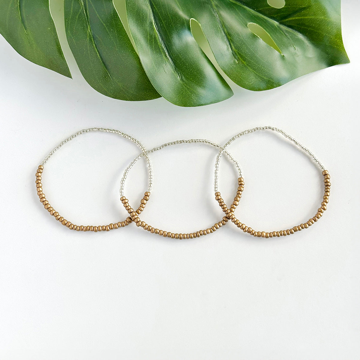 A trio of gold and silver beaded bracelets resting on a bright white background.