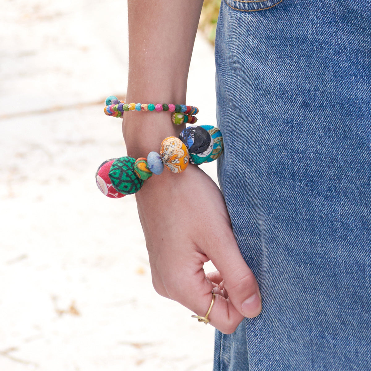 A woman in a denim skirt holds her hand by her side, displaying her vibrant beaded bracelets.