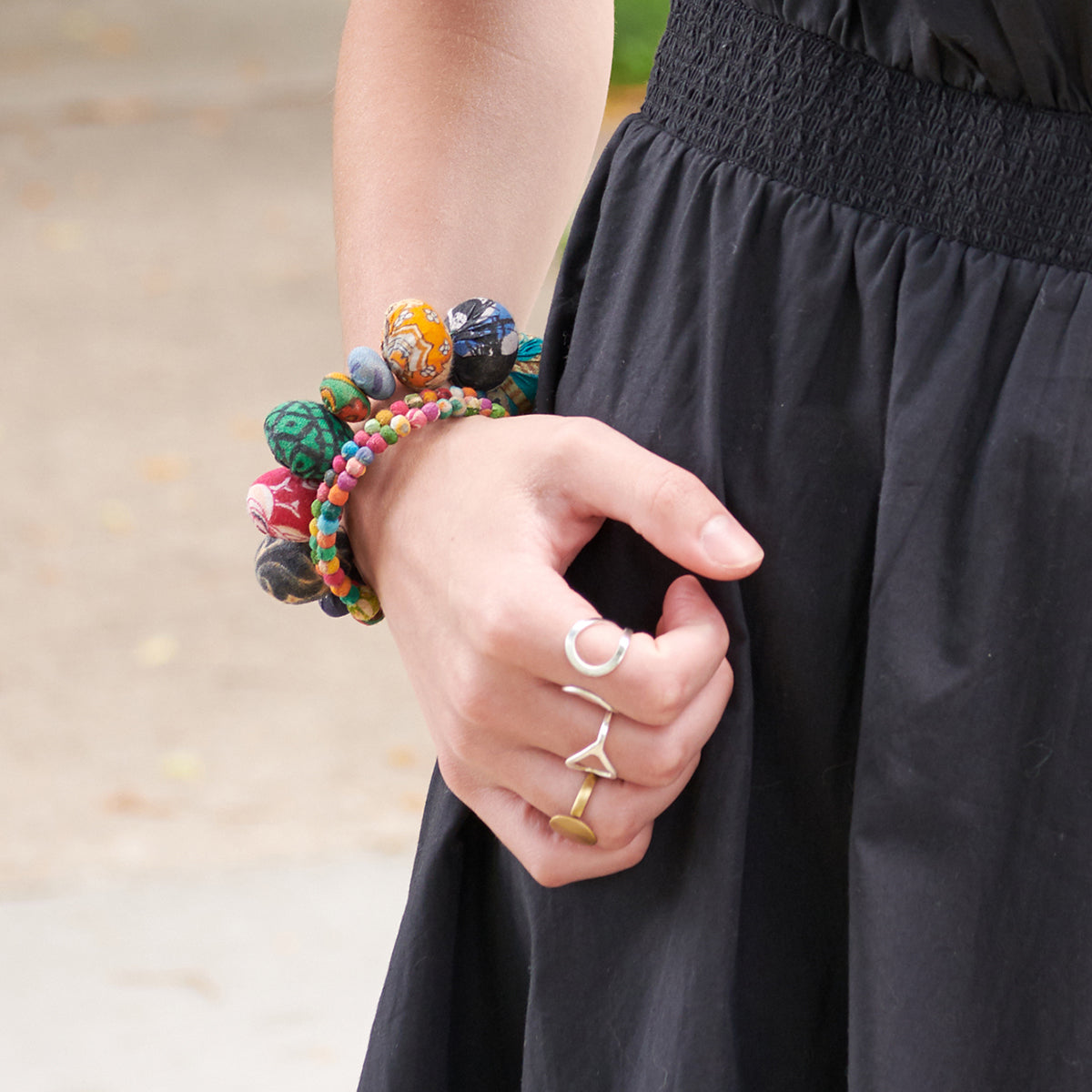 A woman in a black dress holds her hand by her side, displaying her vibrant beaded bracelets.