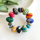 A multicolor beaded bracelet rests on a plate on a white surface with a green leaf in the background.