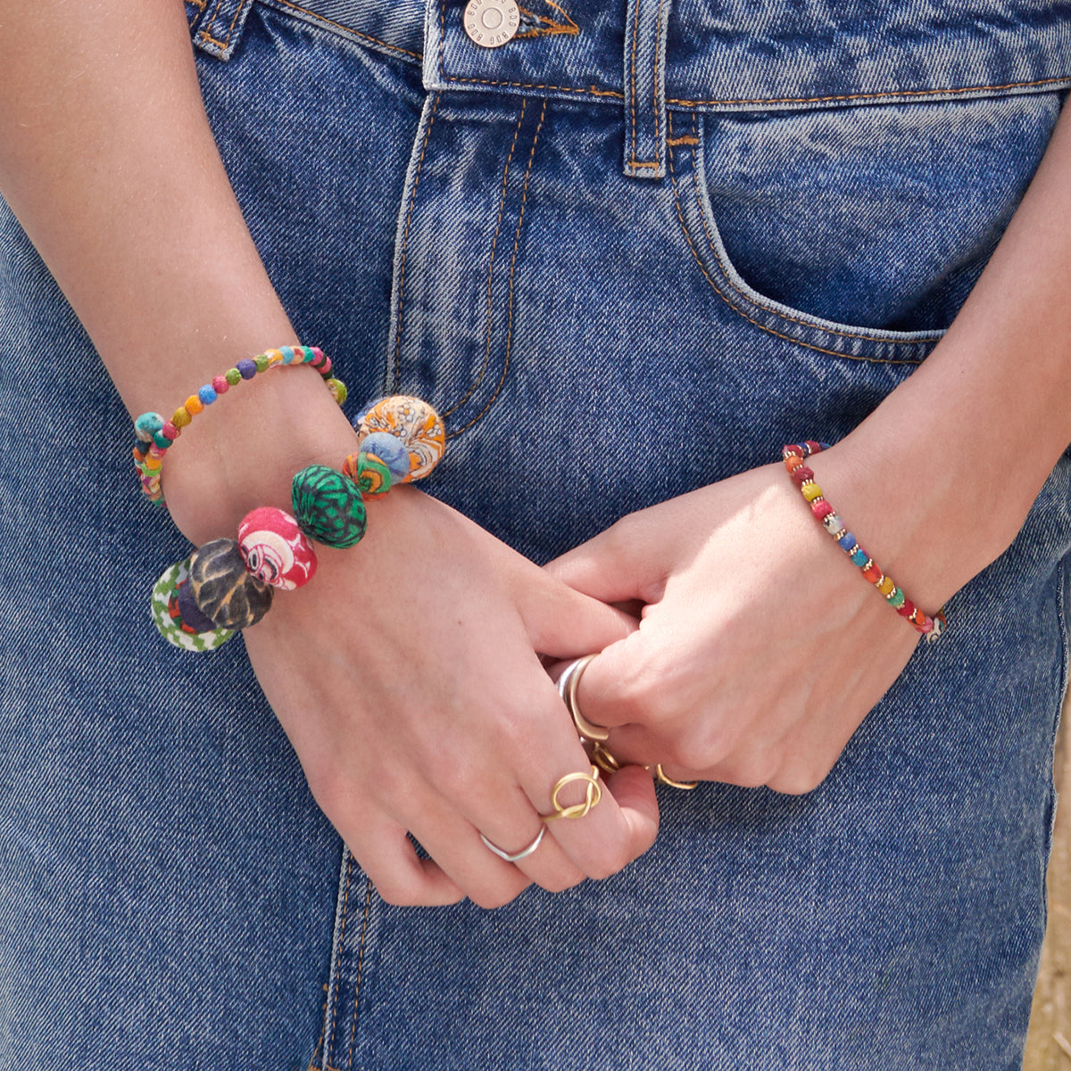 A woman in a denim skirt clasps her hands by her side, displaying her vibrant beaded bracelets.