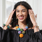 A woman in a black top smiles at the camera while displaying her colorful beaded jewelry.