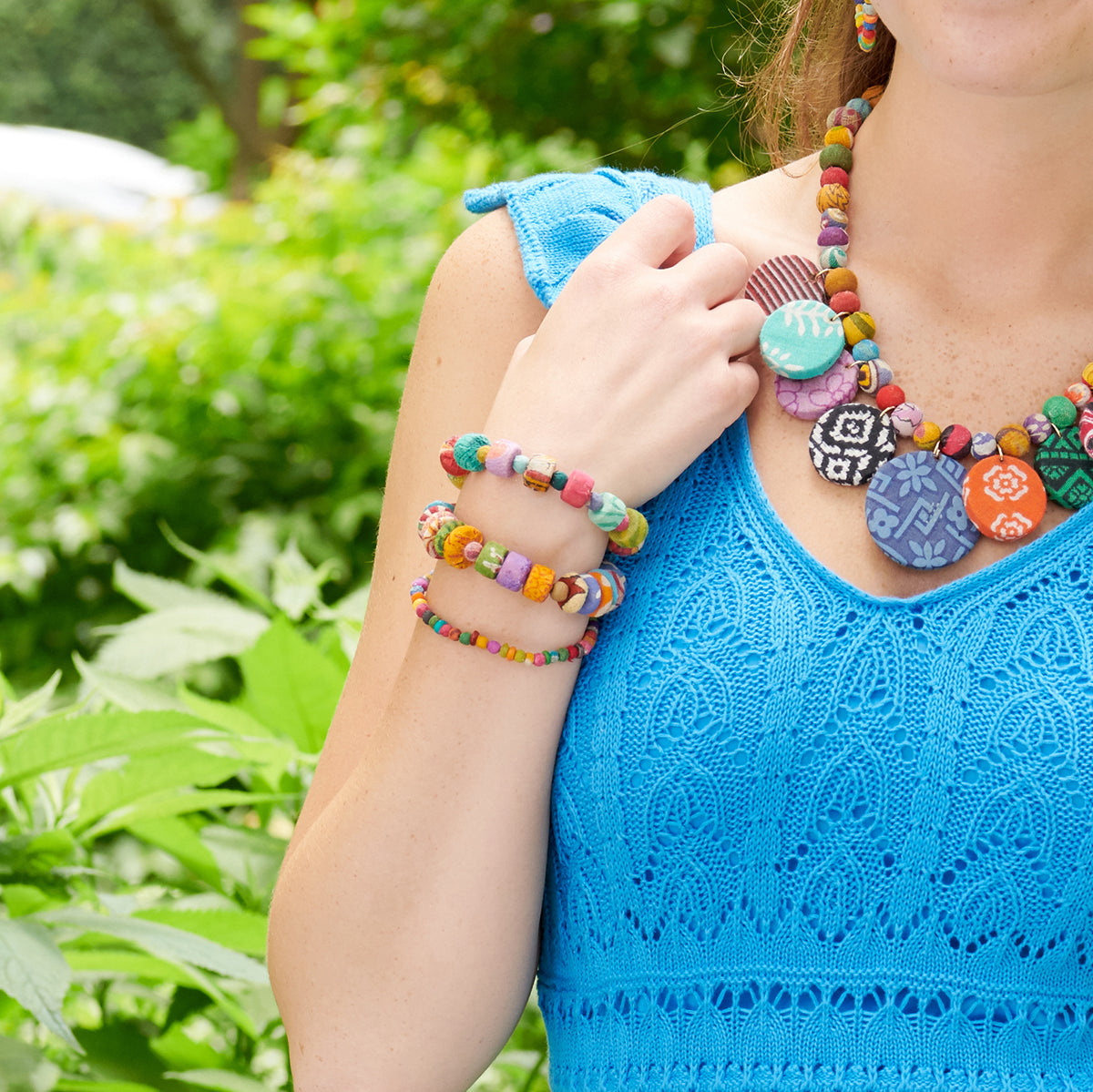 A woman wearing a bright blue dress shows off her wrist, which is adorned with three multicolor beaded bracelets.