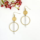 A pair of gold and silver earrings rests on a white background with a red flower in the top corner.