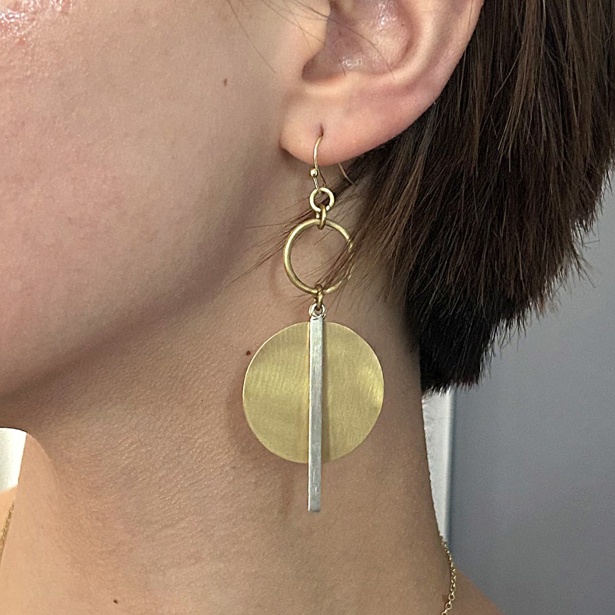 A close up of a gold and silver disc earring in an ear.