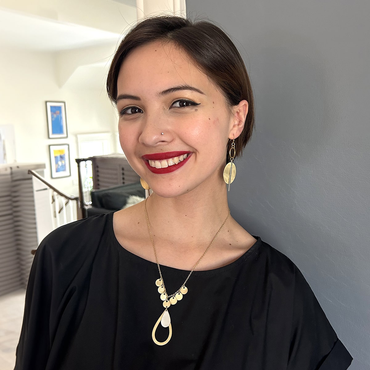 A young woman in a black shirt smiles while showing off her gold and silver jewelry.