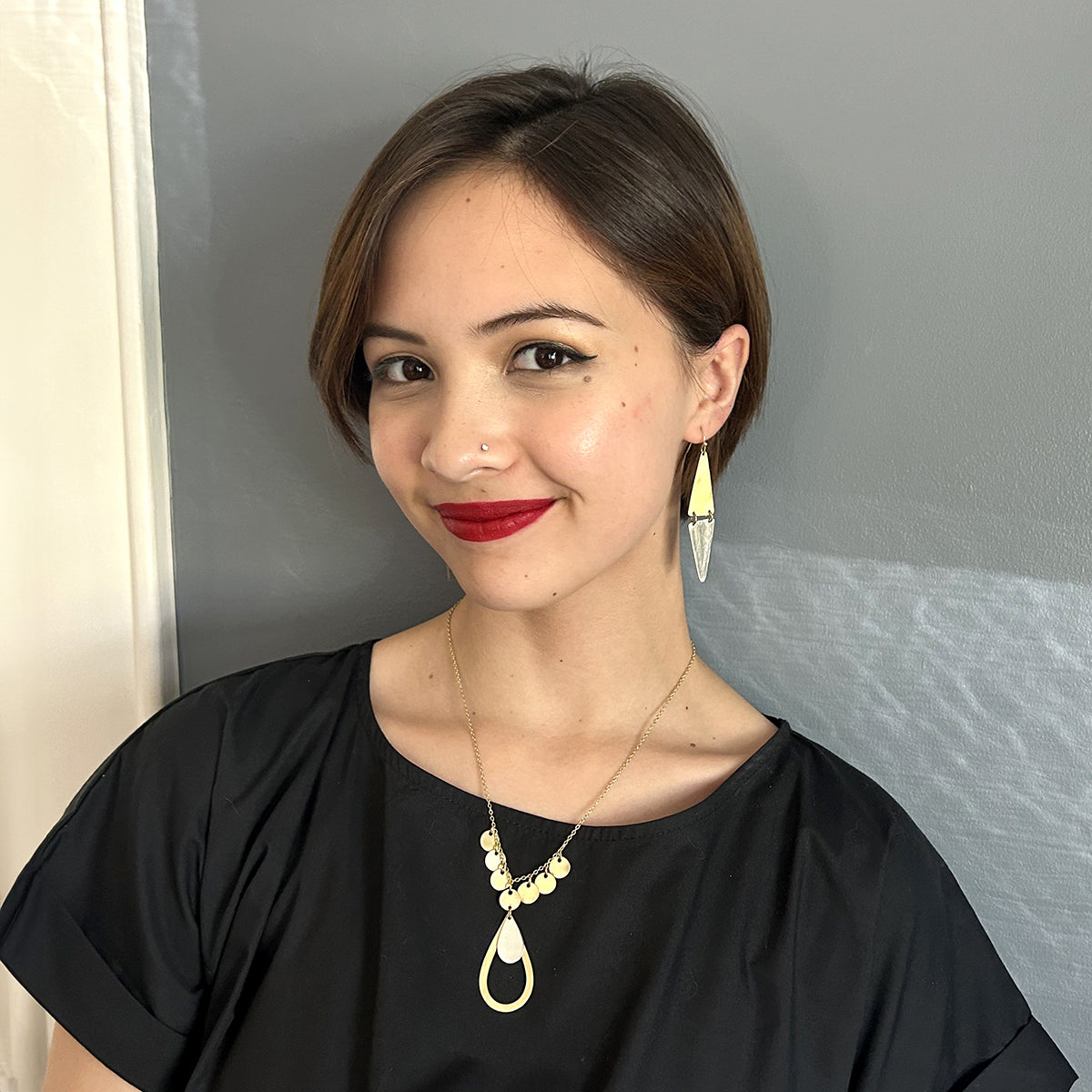 A young woman in a black shirt smiles while showing off her gold and silver jewelry.