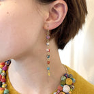 A close up of a woman's ear and her dangling multicolor beaded earrings.