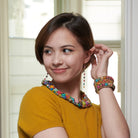 A young woman in a yellow shirt smiles while showing off her multicolor, beaded jewelry.