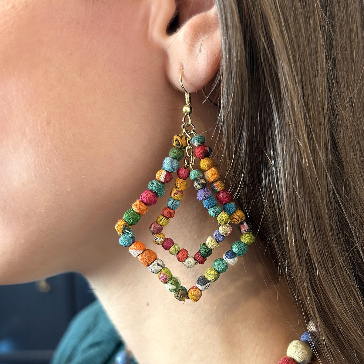 A close up of a woman's ear and her multicolor beaded earring.