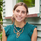 A young woman in a teal shirt smiles while showing off her multicolor, beaded jewelry.