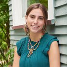 A young woman in a teal shirt smiles while showing off her multicolor, beaded jewelry.