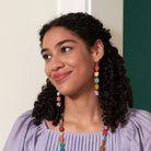 A young woman in a purple shirt softly looks to the left, while showing off her multicolor, beaded jewelry.