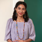 A young woman in a purple shirt smiles while showing off her multicolor, beaded jewelry.