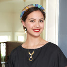 A woman in a black dress is smiling, while modeling a shiny gold pendant necklace and matching earrings.