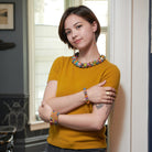 A woman in a yellow top poses confidently while showcasing her multicolored beaded jewelry.