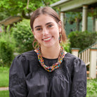 A young woman wearing a black dress stands outside. She is accessorized with a set of multicolor, beaded jewelry.