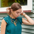 A young woman wearing a teal top looks down while touching the side of her head. She is accessorized with an array of multicolor, beaded jewelry.