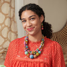 A young woman wearing a bright red shirt smiles while wearing colorful beaded jewelry.