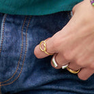 A woman hooks her thumb into her pocket, showing off her gold and silver rings and multicolor beaded bracelet.