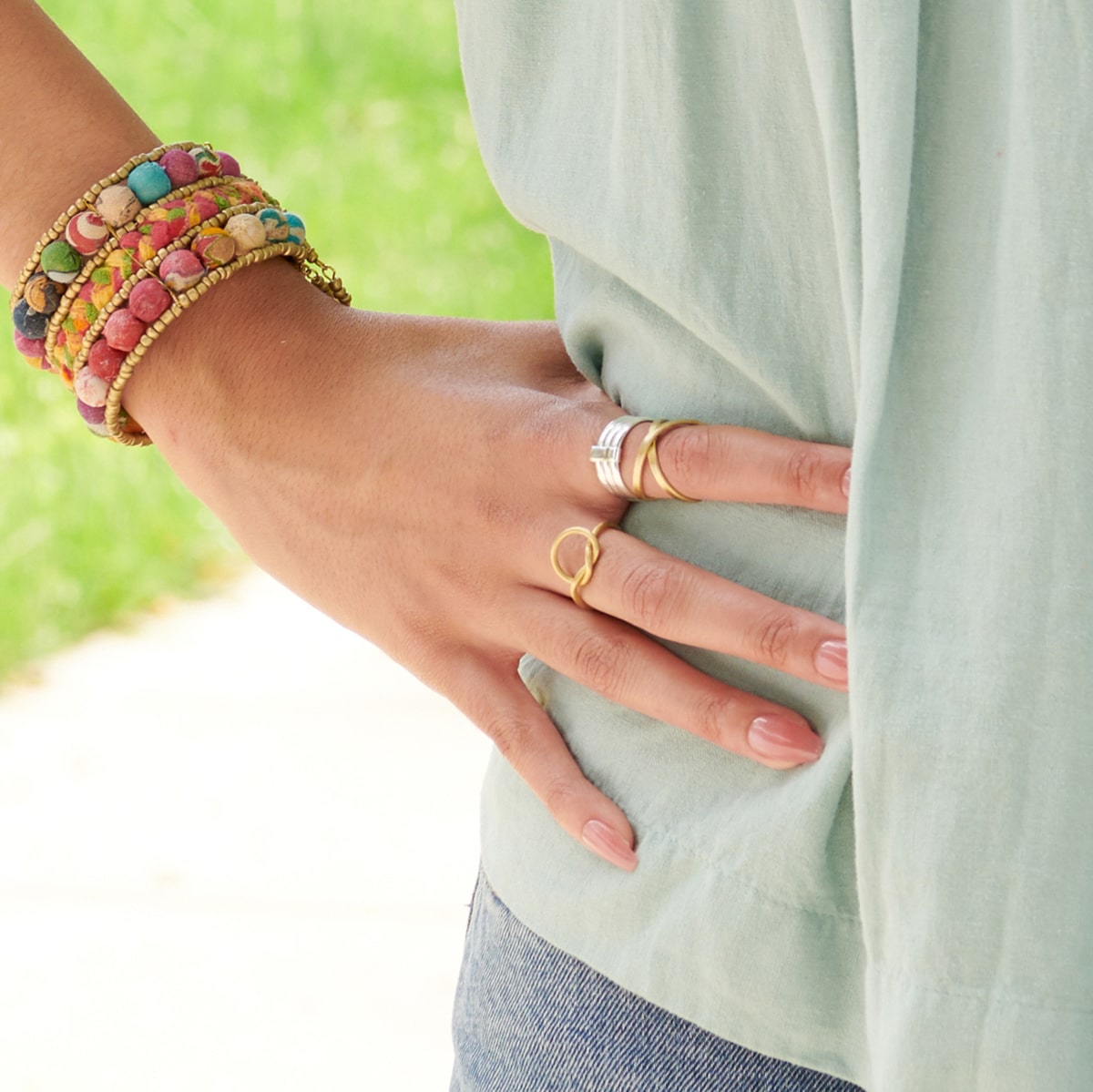 A woman wearing a light blue shirt rests her hand on her hip, showing off her gold and silver rings.