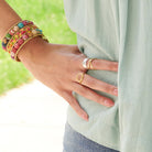 A woman wearing a light blue shirt rests her hand on her hip, showing off her gold and silver rings.