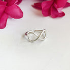 A silver ring with center infinity sign motifs sits against a white surface with a red flower in the background.