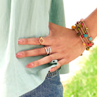 A woman wearing a light blue shirt rests her hand on her hip, showing off her gold and silver rings.