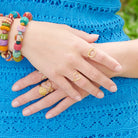 A woman wearing a blue dress holds her hands to her side, showing off the many gold rings on her fingers.