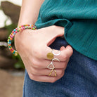 A woman hooks her thumb into her pocket, showing off her gold and silver rings and multicolor beaded bracelet.