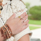 A woman's hand rests on her shoulder, showing off her gold and silver rings.