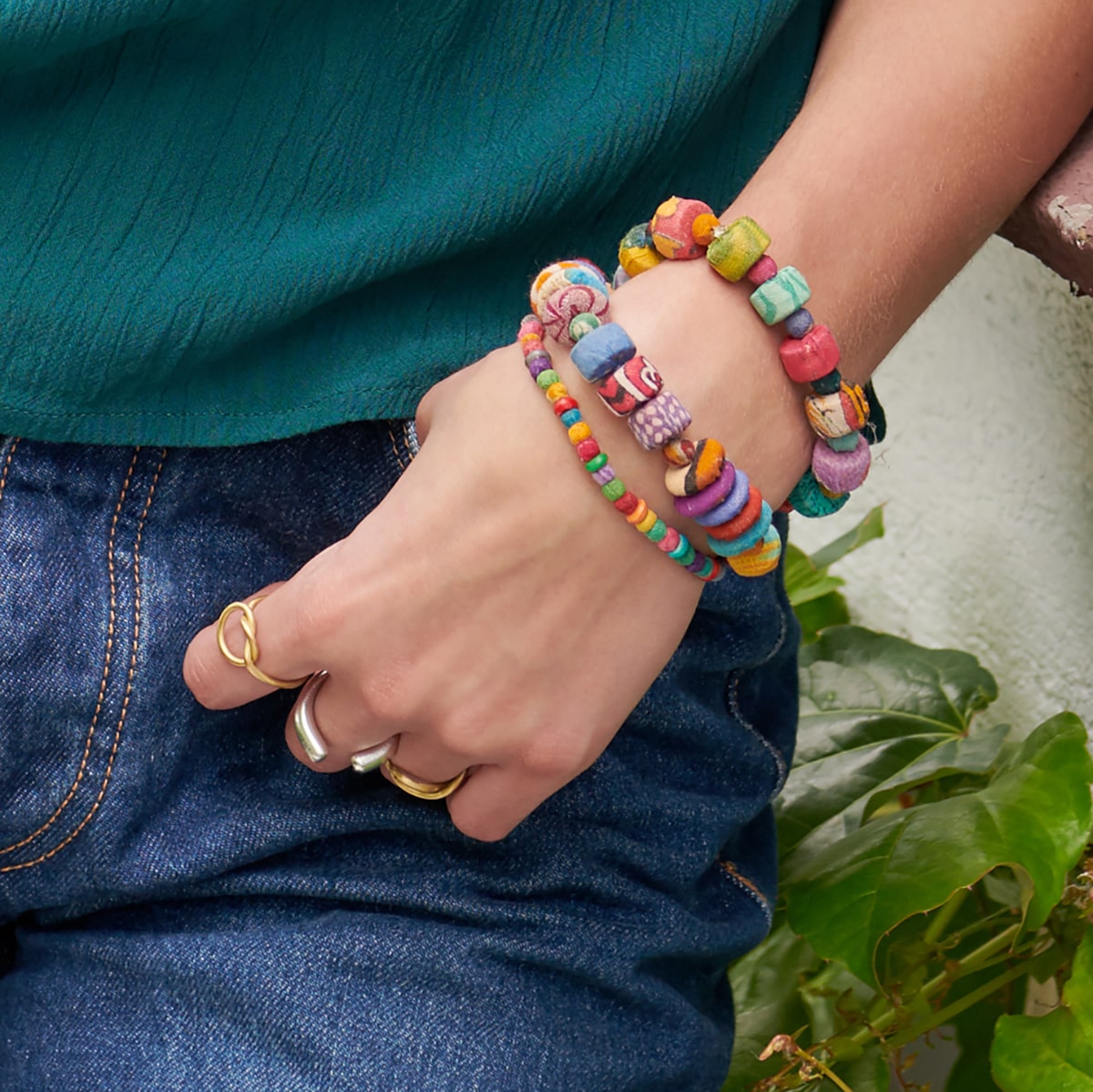 A woman hooks her thumb into her pocket, showing off her multicolor beaded bracelets and silver and gold rings.