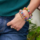 A woman hooks her thumb into her pocket, showing off her multicolor beaded bracelets and silver and gold rings.