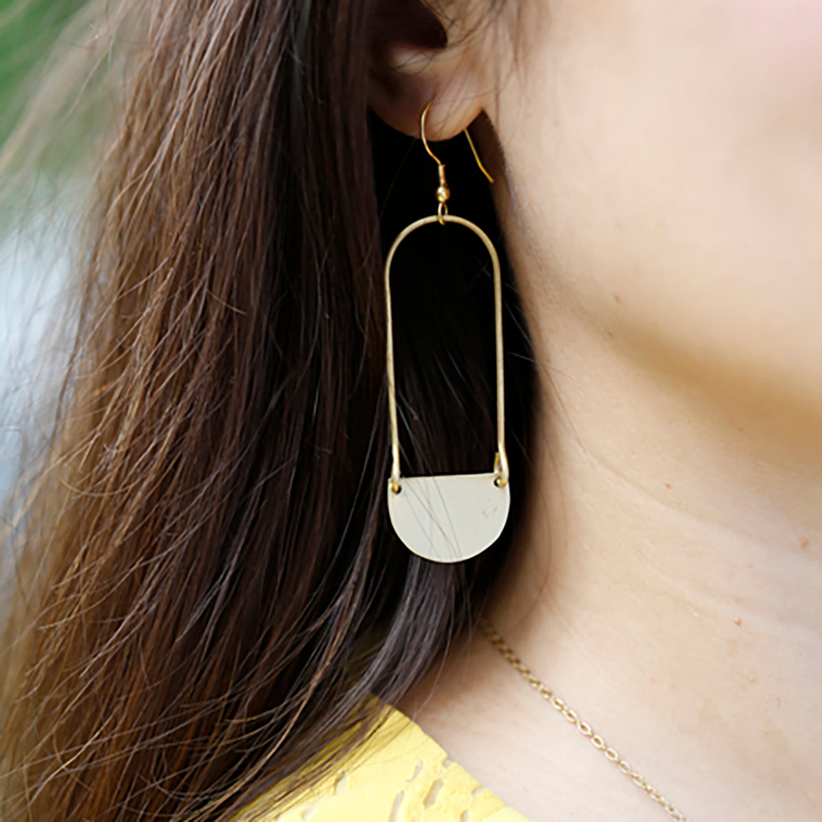 A close up of a gold dangling earring on a woman's ear.