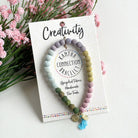 A pastel beaded bracelet tied to a card that reads "Creativity" against a white background with a green leaf to the left.