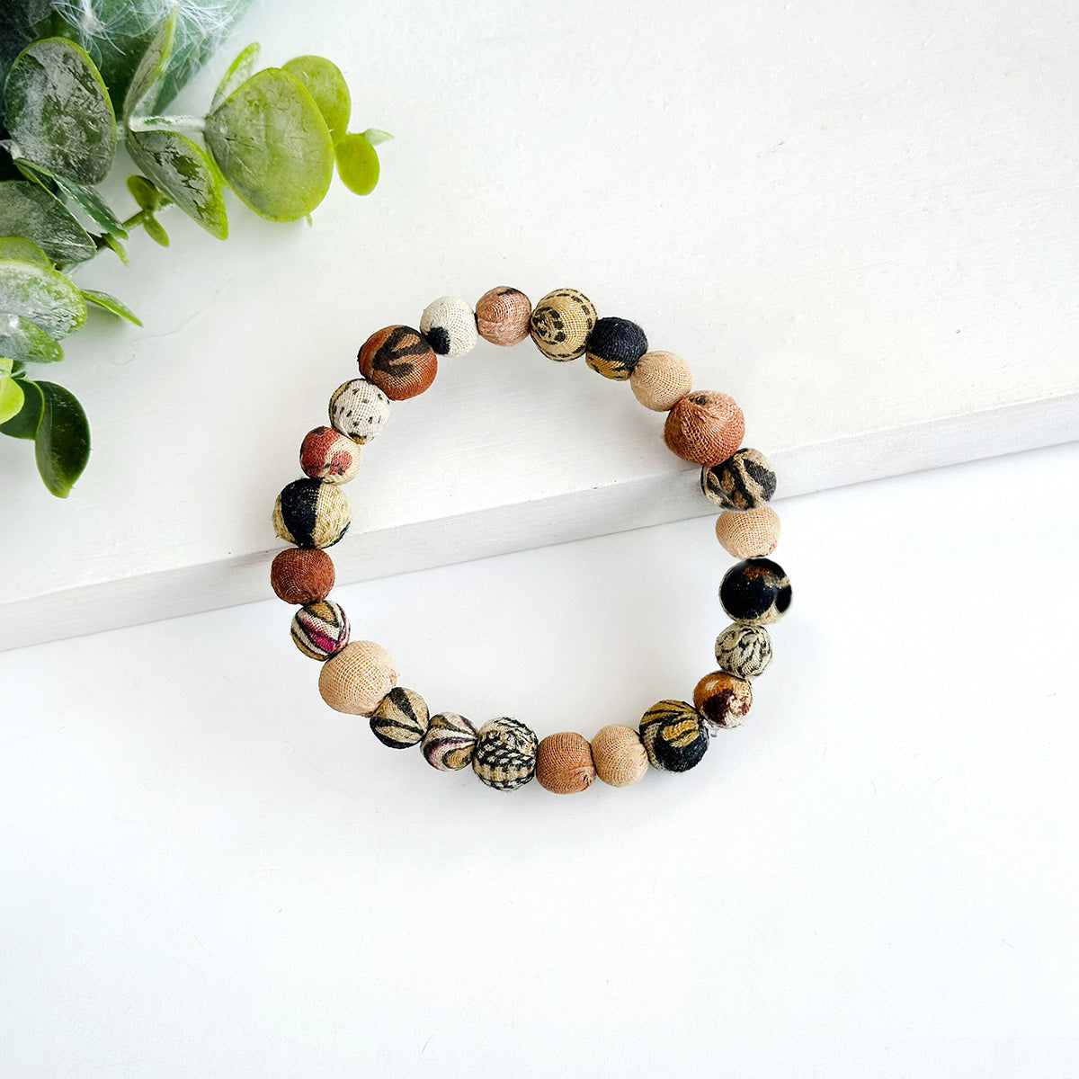 A beaded, neutral-toned bracelet rests on a white background.