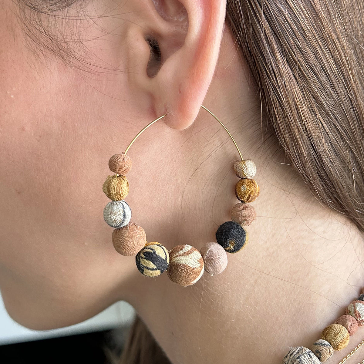 A close up of a woman's ear and the beaded, neutral-toned earring she is wearing.