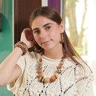 A woman in a crocheted top and beaded jewelry smiles softly at the camera while holding her hand to her ear.