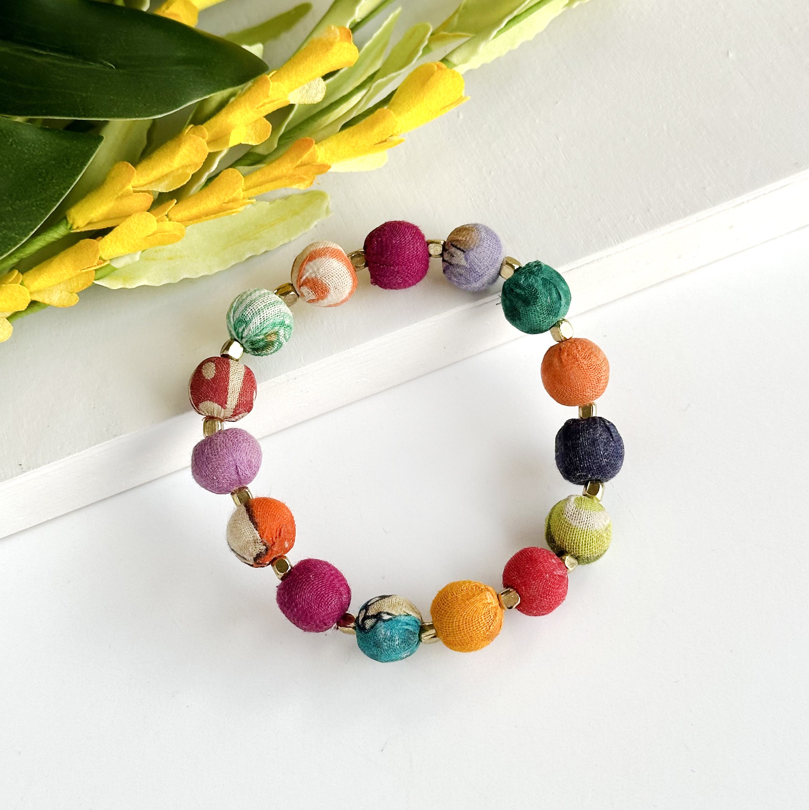 A multicolor beaded bracelet is shown against a white background with a white and green flower.