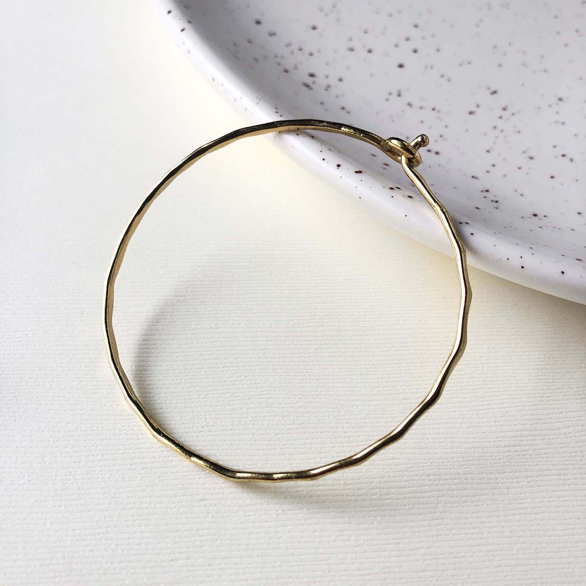 A simple gold band bracelet rests on a white speckled plate.