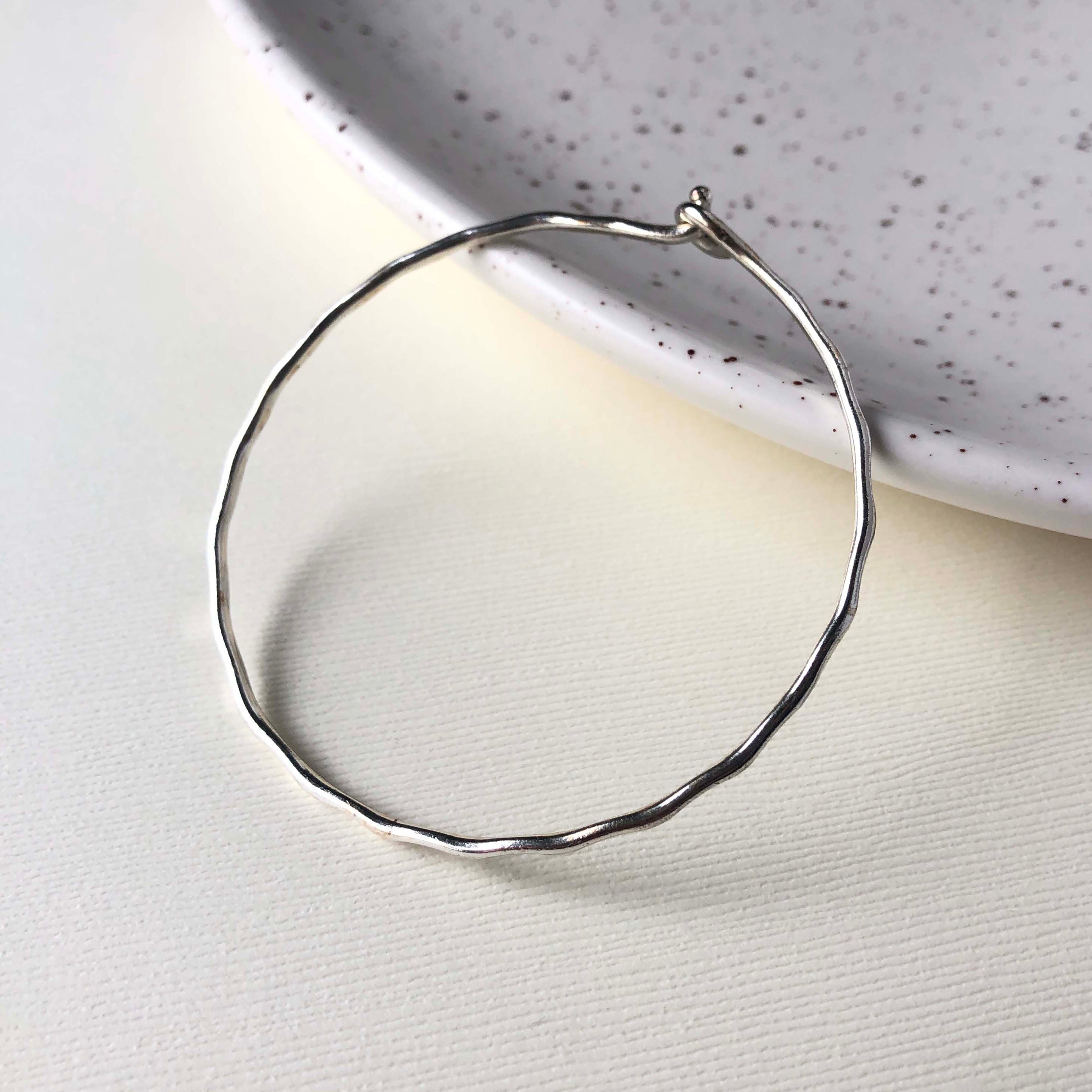 A simple silver band bracelet rests on a white speckled plate.