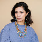 A woman in a periwinkle blue shirt is adorned with multicolored beaded jewelry.