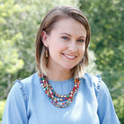 A woman in a blue shirt is adorned with multicolored beaded jewelry.