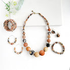 A grouping of beaded neutral-toned bracelets, earrings and a necklace rest against a white background with a succulent as an accent.