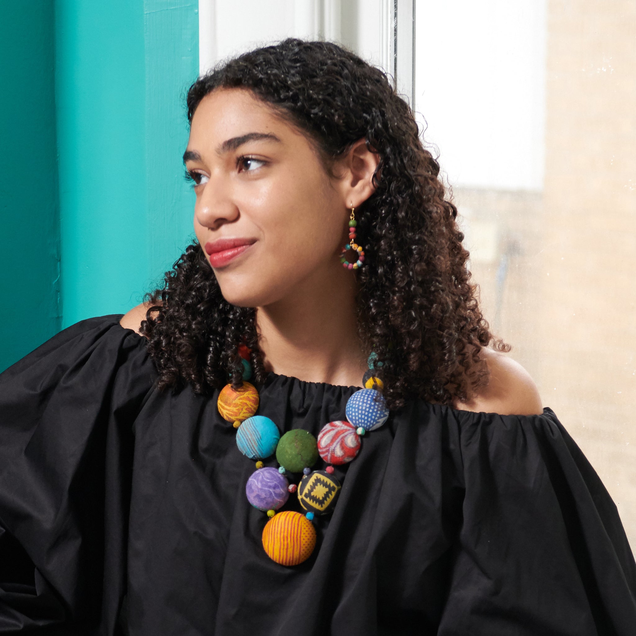 A woman in a black shirt and colorful beaded jewelry looks to the left.