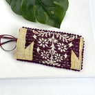 A plum & yellow eyeglass case against a white background, with a pair of red eyeglasses sticking out of the pouch.