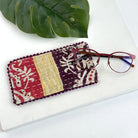 A plum, yellow & red eyeglass case against a white background, with a pair of red eyeglasses resting on top of the pouch.