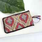 A yellow & red eyeglass case against a white background, with a pair of red eyeglasses sticking out of the pouch.