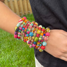 A close up of a woman's wrist and the 12 beaded multicolor bracelets she is wearing.