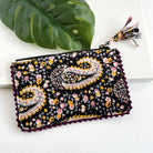 A black floral-patterned rectangular pouch against a white background with a large leaf in the background.